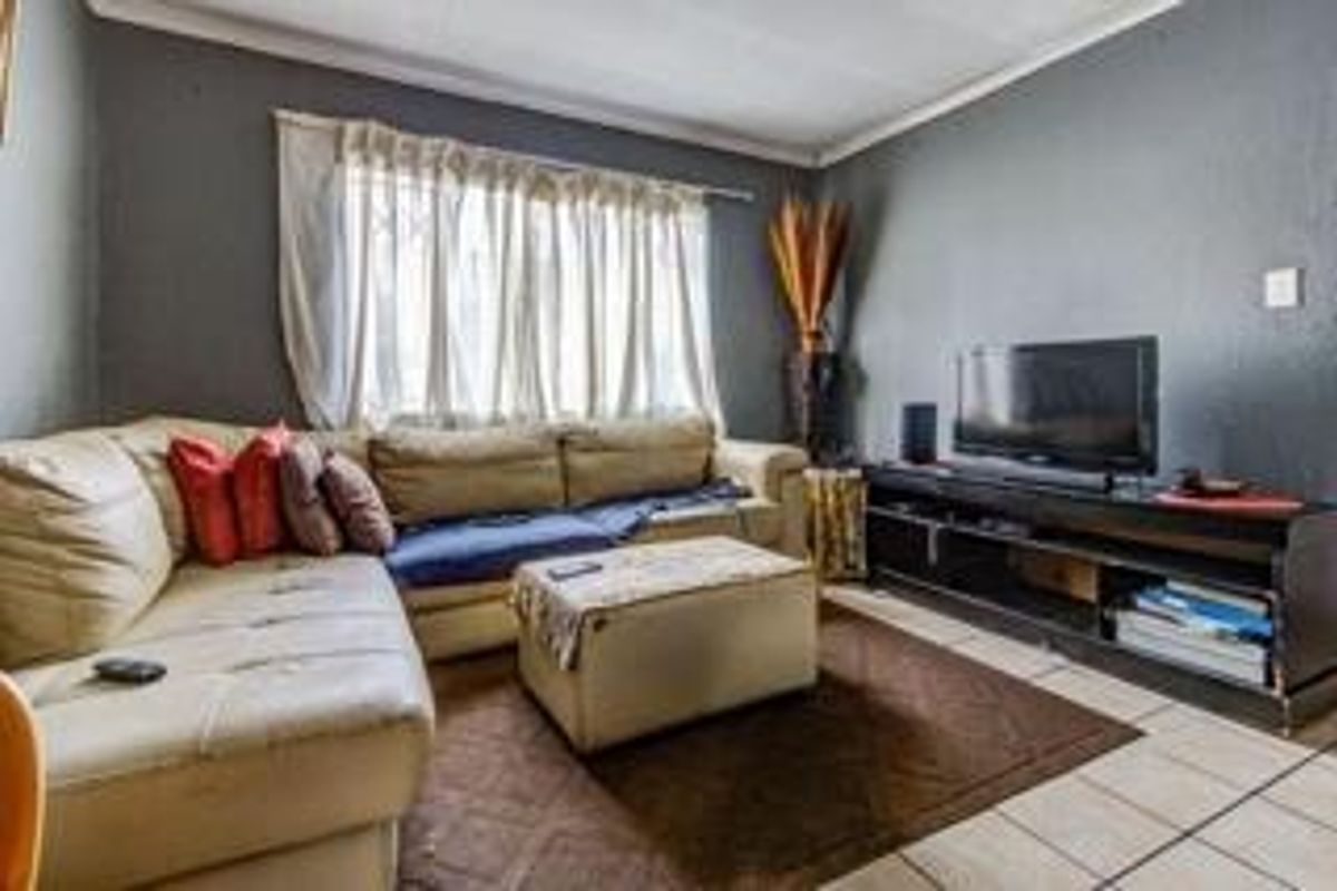 A living room featuring tiled flooring, coving, and a window with curtain rod, providing a functional space for relaxation.