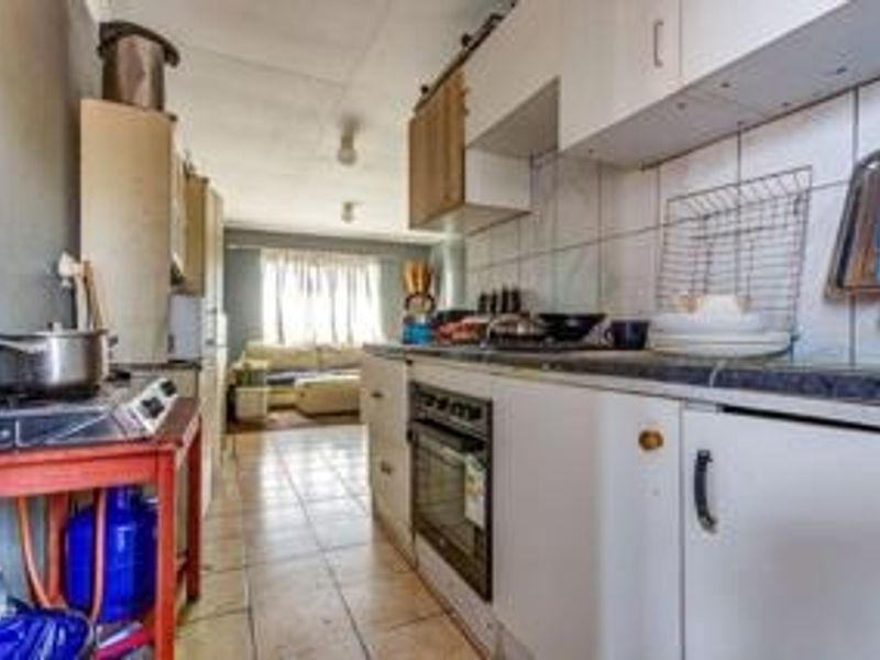 A functional galley-style kitchen featuring built-in cabinetry, tiled backsplash, and an integrated oven, leading into an open-plan living area.