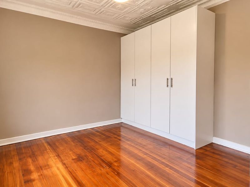 A bright, empty bedroom featuring polished hardwood floors, built-in white cupboards, and decorative ceiling detailing.