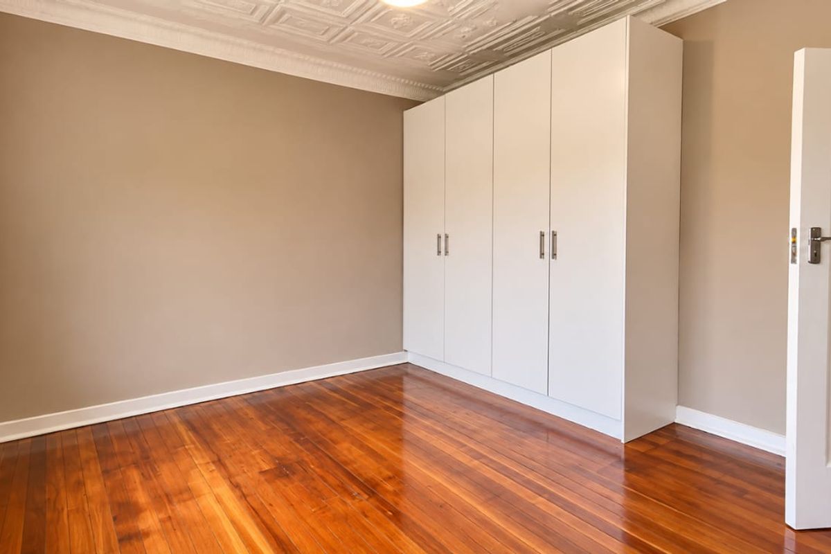 A bright, empty bedroom featuring polished hardwood floors, built-in white cupboards, and decorative ceiling detailing.