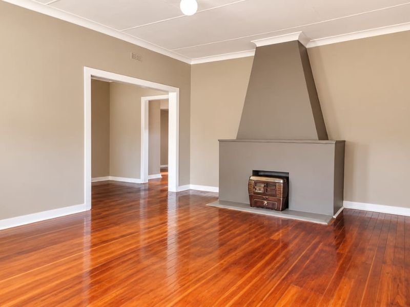 Spacious living room featuring polished hardwood flooring, neutral wall tones, and a prominent built-in fireplace with a modern surround.