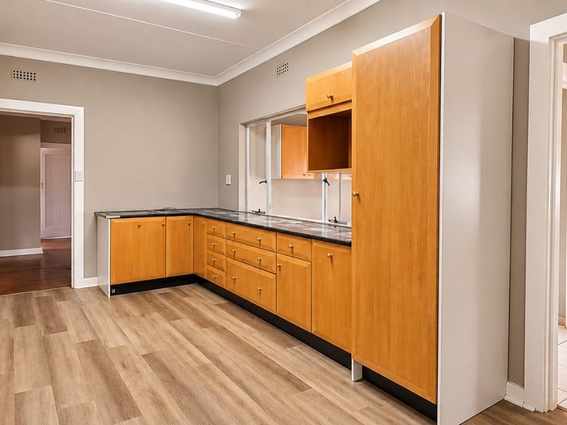 A functional scullery or prep area featuring wood-look laminate cabinetry, ample counter space, and a tall built-in pantry cupboard.