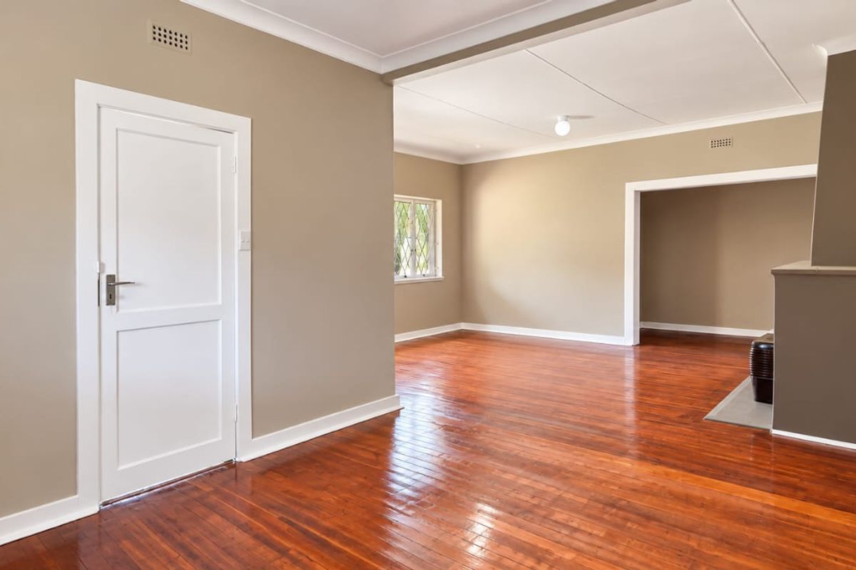 Spacious, light-filled living area featuring polished hardwood flooring, neutral wall tones, and a classic fireplace hearth, offering a versatile blank canvas.