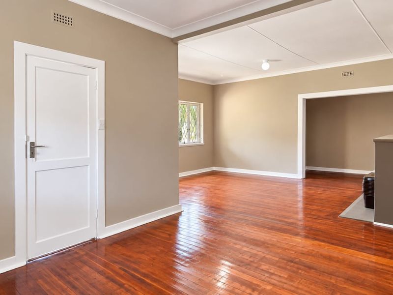 Spacious, light-filled living area featuring polished hardwood flooring, neutral wall tones, and a classic fireplace hearth, offering a versatile blank canvas.