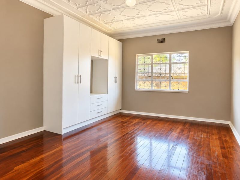 A bright, empty bedroom featuring polished hardwood floors, a built-in wardrobe, and an ornate decorative ceiling.