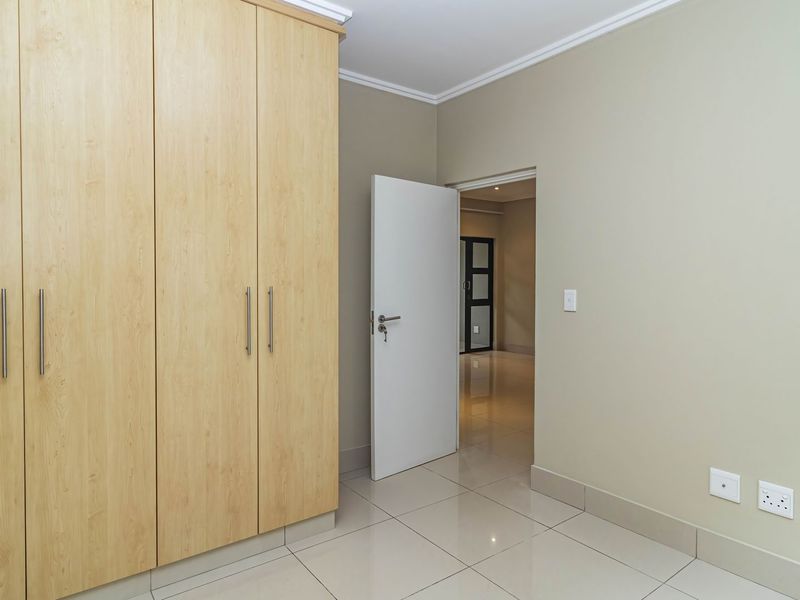 A clean, empty bedroom featuring light wood-finish built-in cupboards, neutral wall paint, and polished floor tiles.