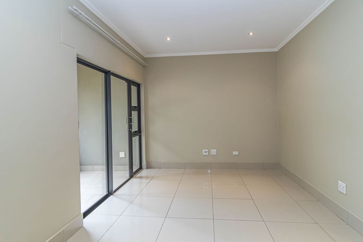 A bright, empty living area featuring neutral tiled flooring, recessed lighting, and a sliding glass door providing access to an outdoor space.