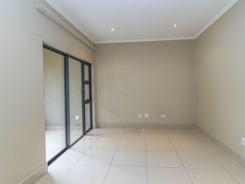 A bright, empty living area featuring neutral tiled flooring, recessed lighting, and a sliding glass door providing access to an outdoor space.