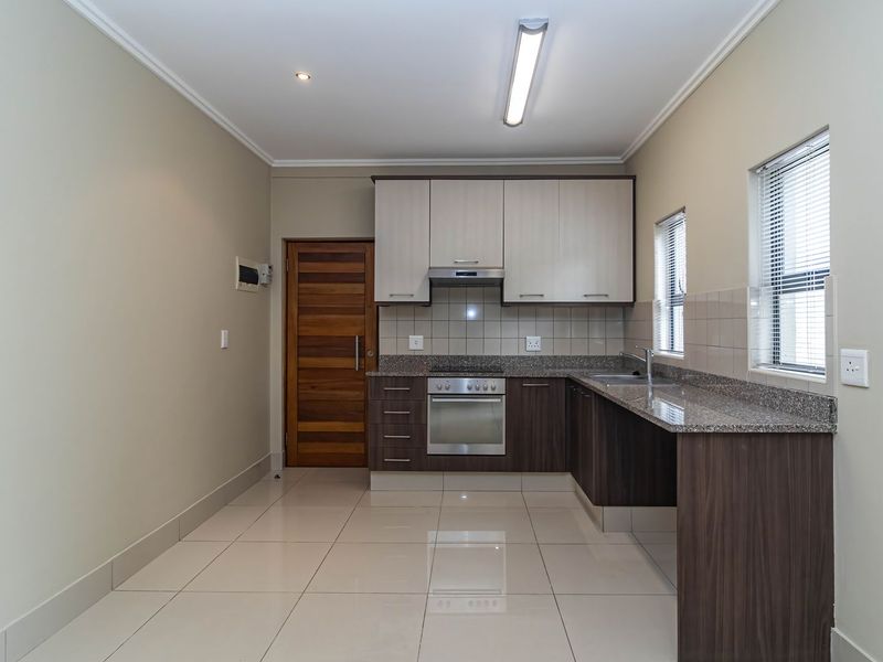 A clean, modern kitchen featuring two-tone cabinetry, granite countertops, integrated stainless steel appliances, and neutral tiled flooring.