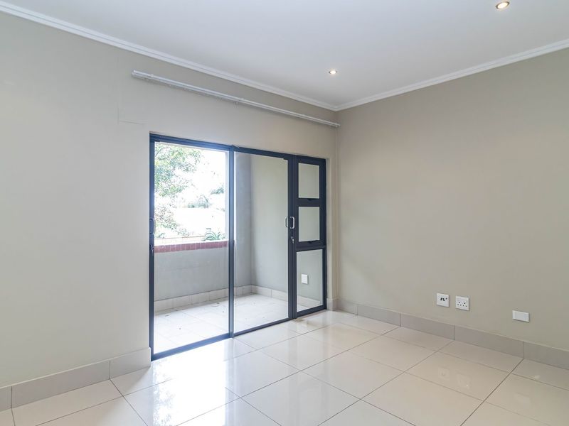 A bright, empty living area featuring neutral walls, tiled flooring, and a sliding glass door providing access to an outdoor balcony.