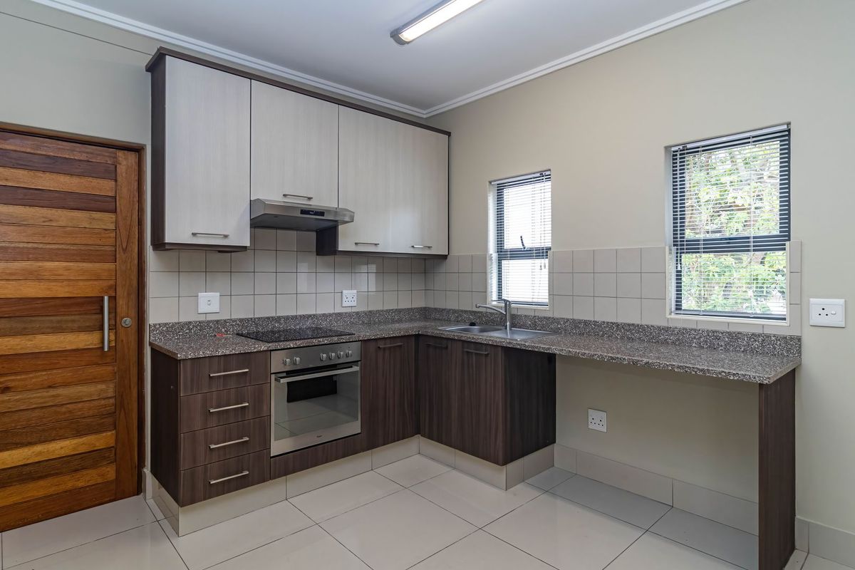 Modern kitchen featuring two-tone cabinetry, granite countertops, integrated oven and hob, and tiled flooring with ample natural light.