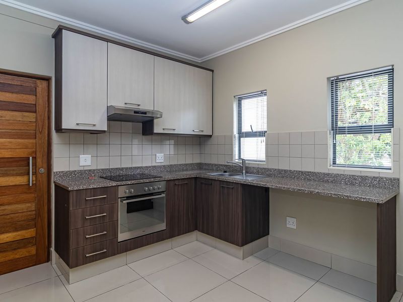 Modern kitchen featuring two-tone cabinetry, granite countertops, integrated oven and hob, and tiled flooring with ample natural light.