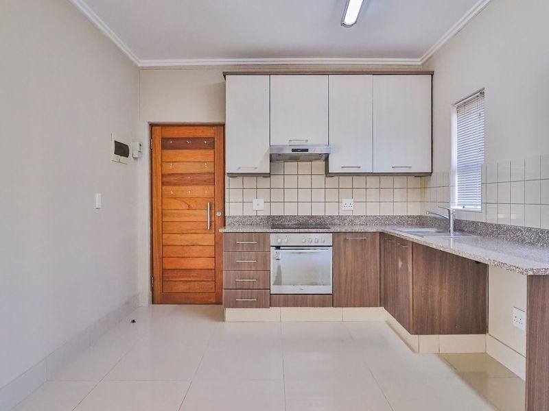 A clean and functional kitchen featuring modern wood-finish cabinetry, granite countertops, built-in oven and hob, and neutral tiled flooring.