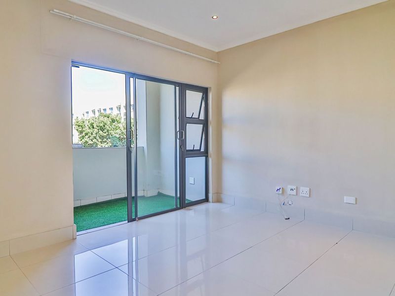 A bright, empty living room featuring polished tile floors, recessed lighting, and a large sliding glass door providing access to a private balcony.