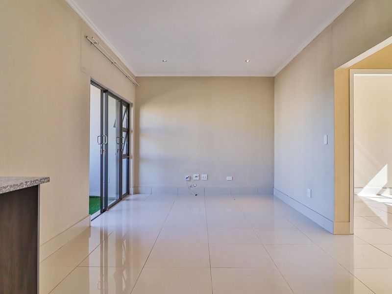 A bright, empty living area featuring polished tiled floors, recessed lighting, and a sliding glass door providing access to an outdoor space.