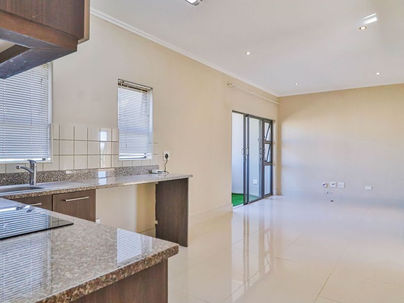A bright, open-plan living and kitchen area featuring modern granite countertops, tiled flooring, and direct access to an outdoor space through sliding glass doors.