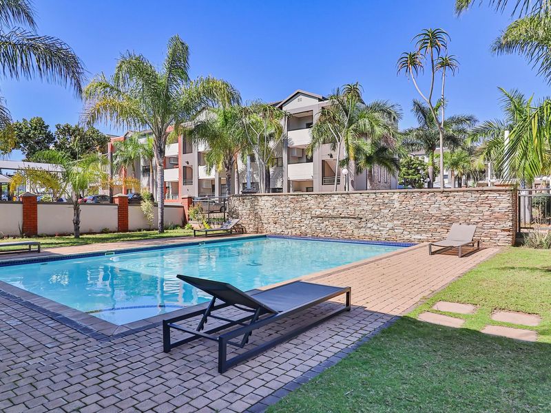 A well-maintained communal swimming pool area featuring a stone-clad feature wall, brick paving, and landscaped garden surrounds within an apartment complex.