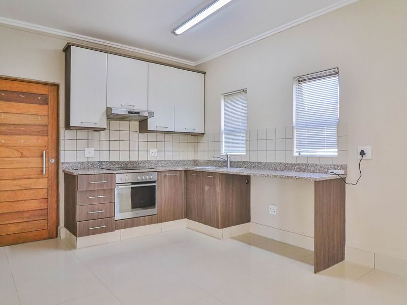 A clean, functional kitchen featuring modern two-tone cabinetry, granite countertops, built-in oven and hob, and tiled backsplash with ample natural light.