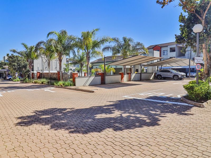 A well-maintained paved parking area within an apartment complex, featuring covered carports, established palm trees, and neat boundary walls.