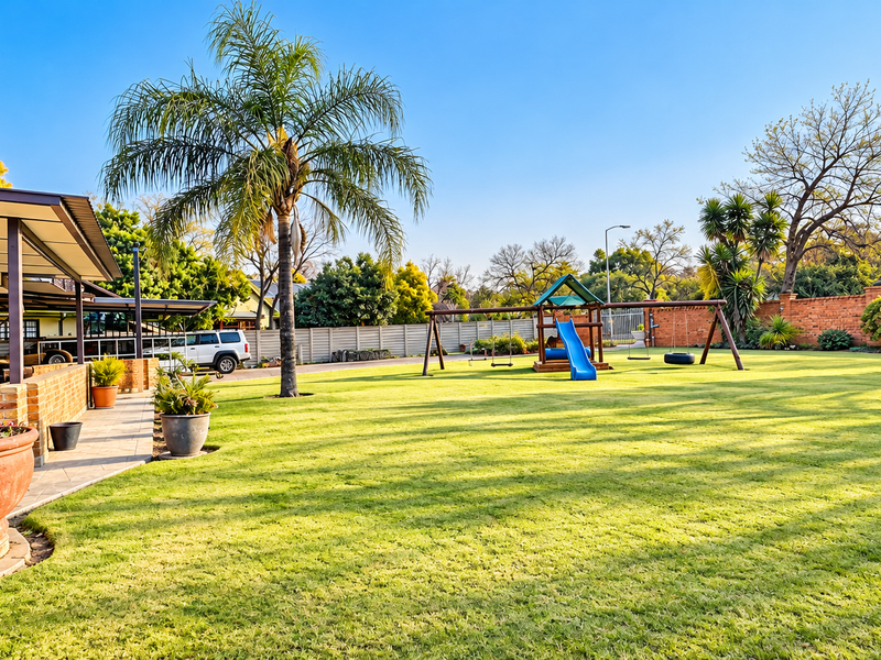 Spacious rear garden featuring a well-maintained lawn, covered patio area, brick boundary walls, and established landscaping.
