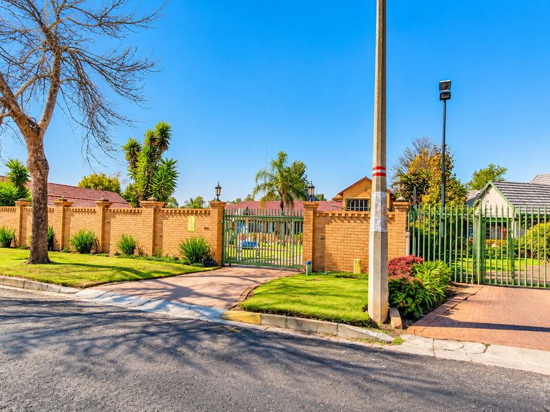 Street view of the property featuring a secure brick boundary wall, metal entrance gates, and a paved driveway leading to the residence.