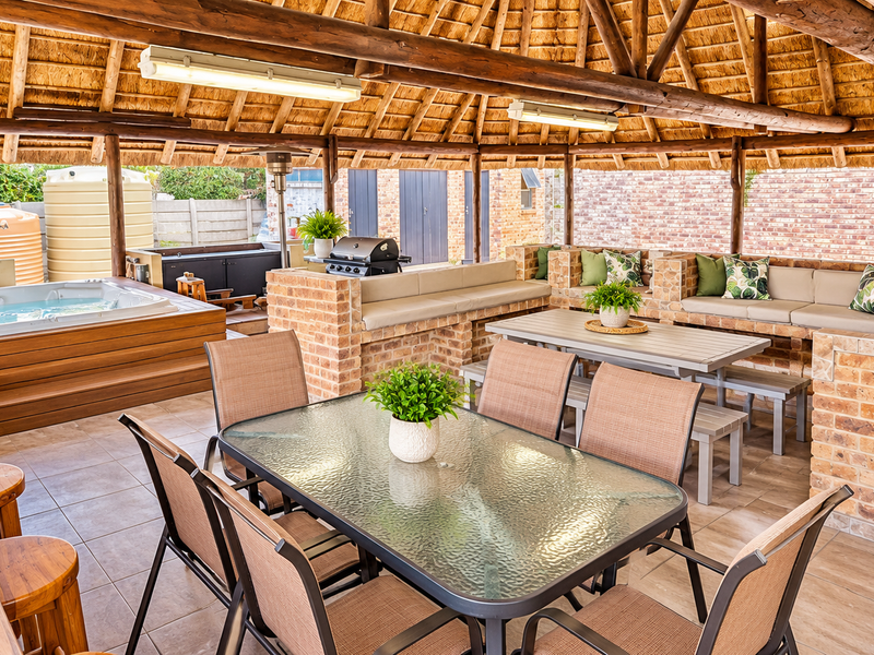 Spacious covered outdoor entertainment area featuring a thatched roof, built-in brick seating, and a private jacuzzi, perfect for hosting guests.