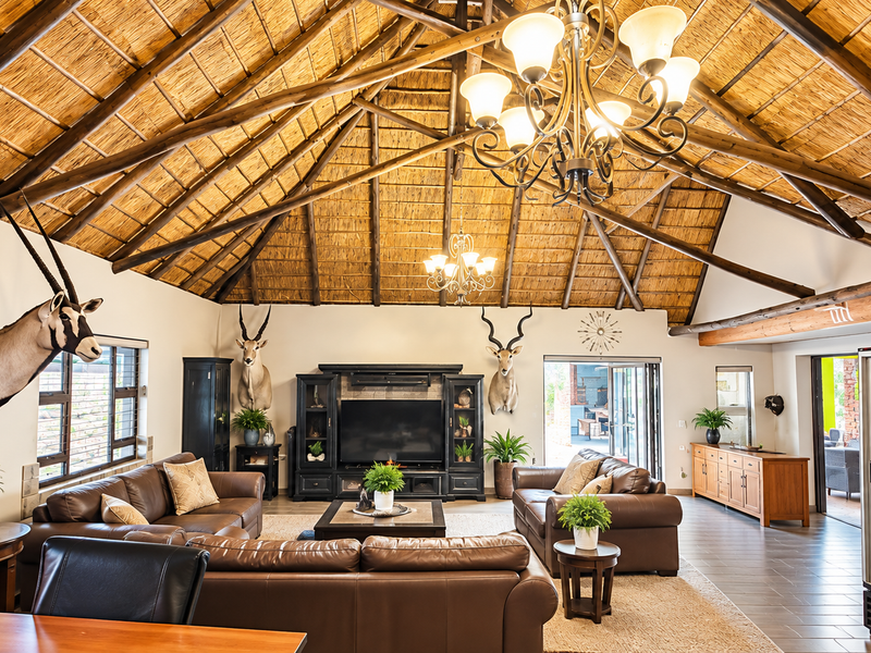 Spacious living area featuring a high vaulted thatched ceiling with exposed timber rafters, stone fireplace, and large stacking doors leading to the patio.
