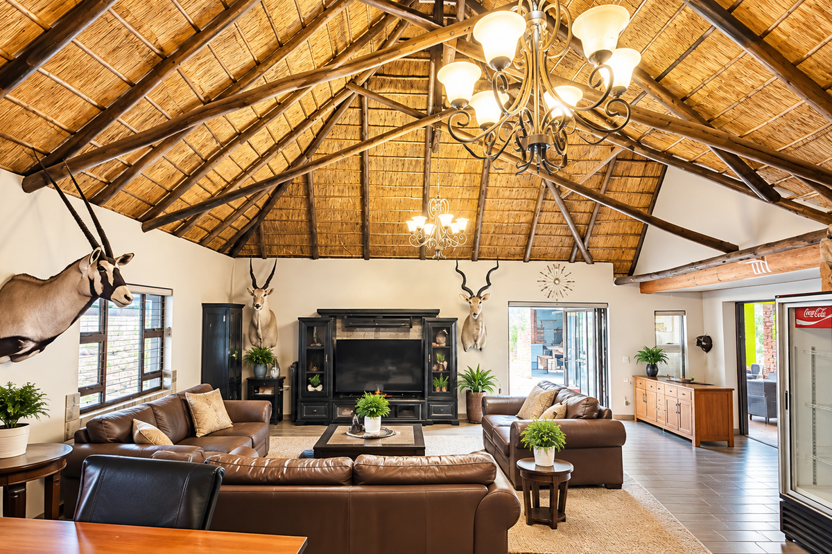 Spacious living area featuring a high vaulted thatched ceiling with exposed timber rafters, stone fireplace, and large stacking doors leading to the patio.