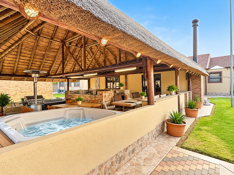 Spacious covered patio featuring a thatched roof, built-in jacuzzi, and brick masonry, overlooking a well-maintained garden area.