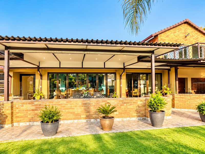 Spacious covered rear patio featuring brick walling, tiled flooring, and recessed lighting, providing a seamless transition between the indoor living areas and the garden.