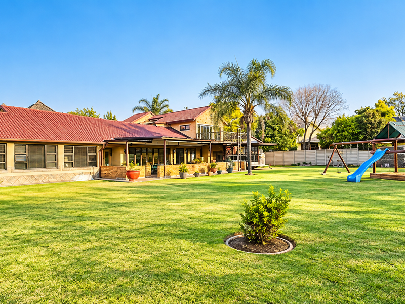 Spacious rear garden featuring a well-maintained lawn, covered patio area, and a multi-level house structure with a tiled roof.