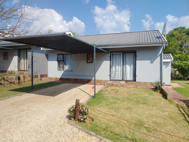Front view of a single-story house featuring a metal roof, a covered carport, and a gravel driveway with a small front lawn.