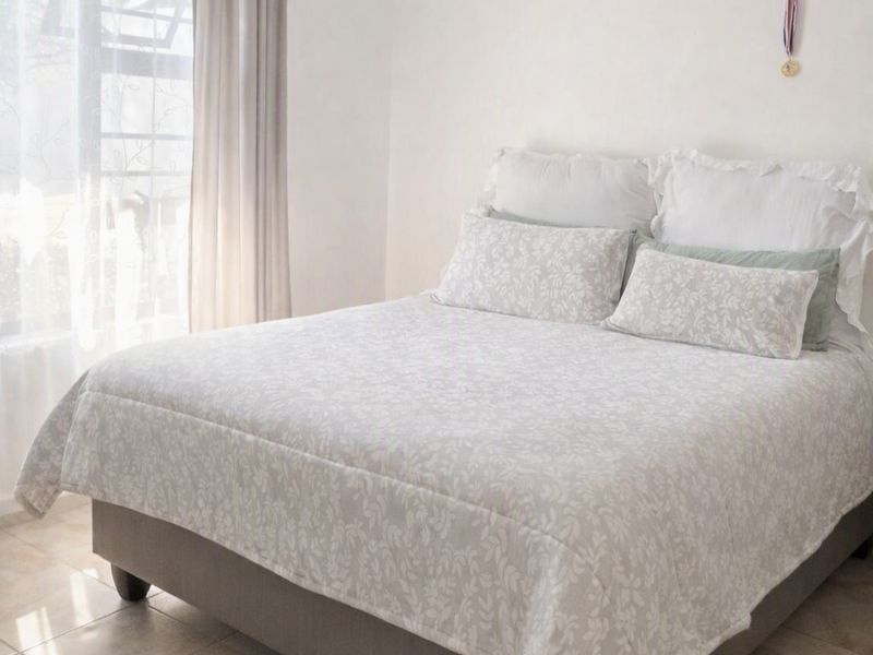 A bright bedroom featuring neutral tiled flooring and a large window allowing for ample natural light.