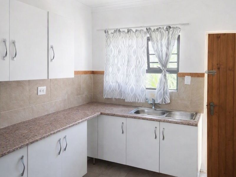 A functional kitchen featuring white cabinetry, laminate countertops, a double bowl stainless steel sink, and a tiled backsplash with a timber door.