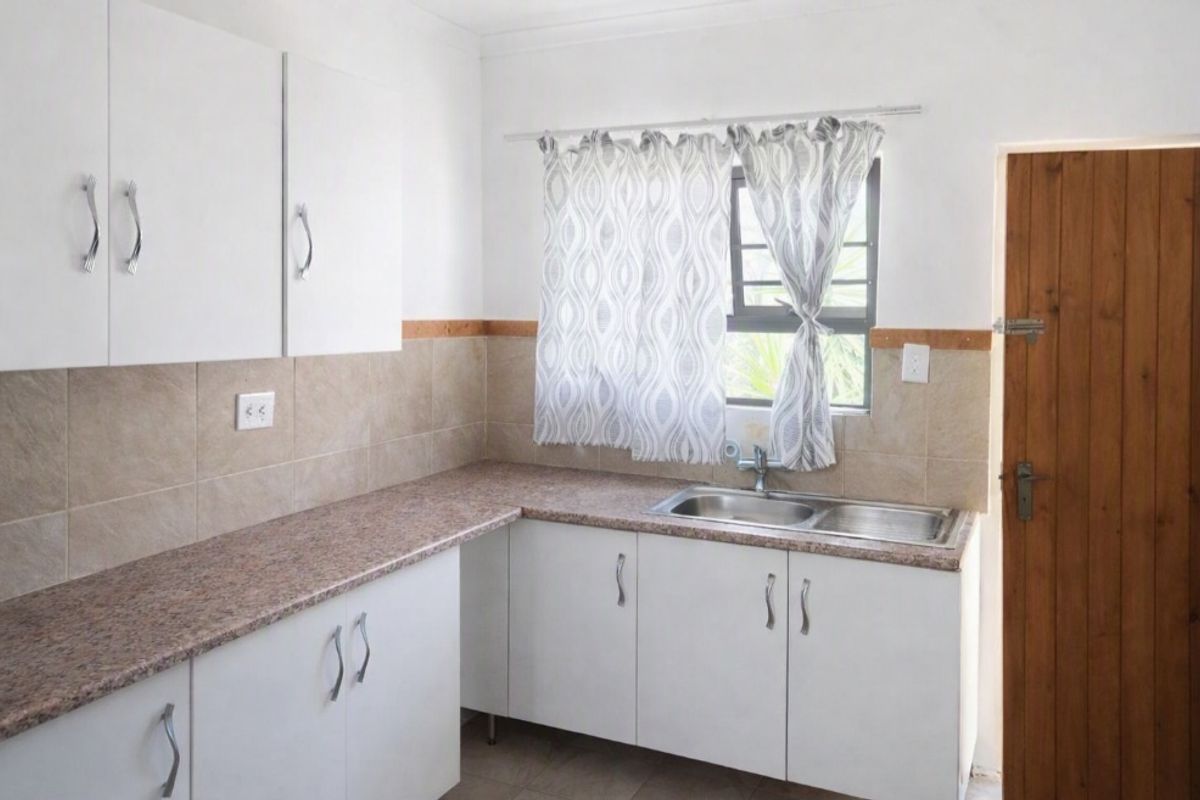 A functional kitchen featuring white cabinetry, laminate countertops, a double bowl stainless steel sink, and a tiled backsplash with a timber door.