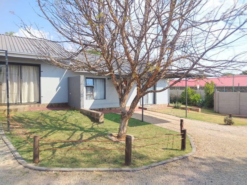 Front view of the property featuring a gravel driveway, metal roof, and established garden area with perimeter fencing.