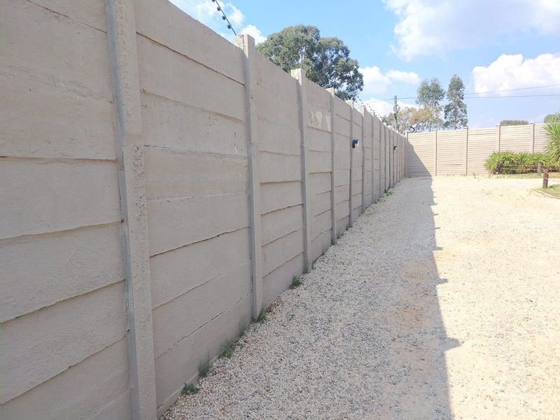 A view of a long precast concrete boundary wall with electric fencing, bordering a gravel driveway area.