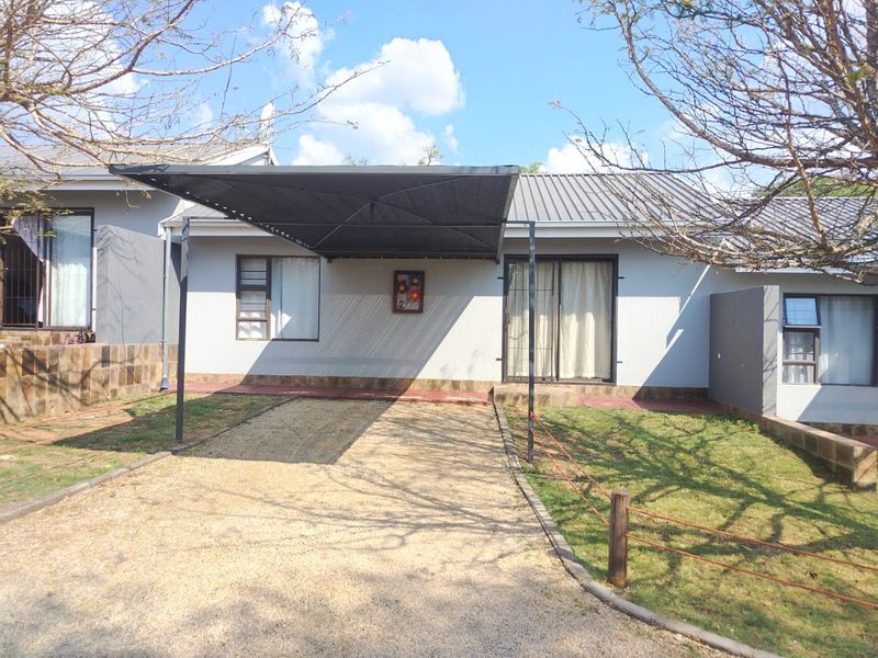 Front view of the property featuring a gravel driveway, a covered carport, and a neutral-toned facade with aluminium window frames and sliding door access.