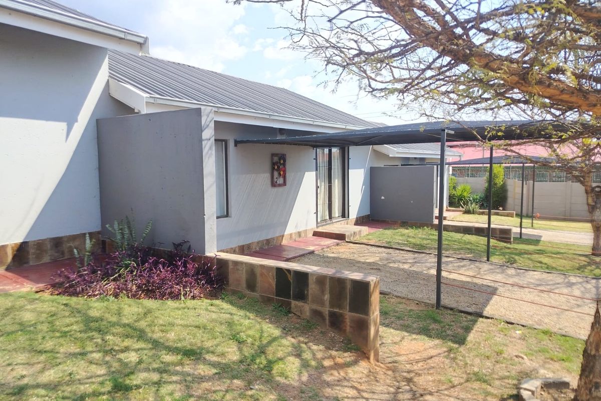 Rear exterior view of the house featuring a metal roof, a covered carport area, and a paved patio space with a low retaining wall.