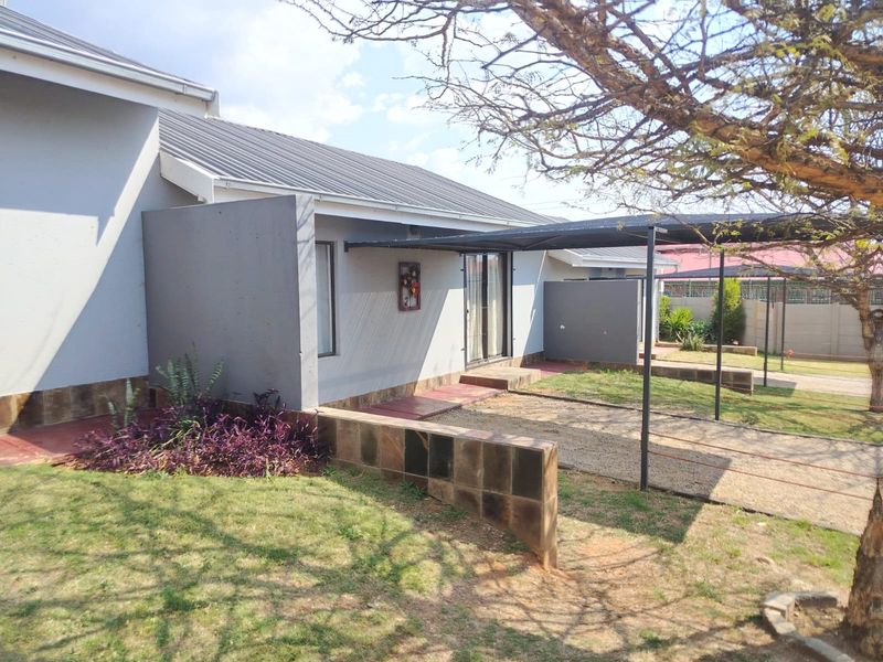 Rear exterior view of the house featuring a metal roof, a covered carport area, and a paved patio space with a low retaining wall.