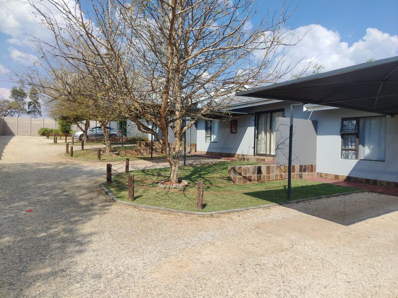 Front exterior view of the property featuring a gravel driveway, carport, and landscaped garden area with tiled retaining walls.