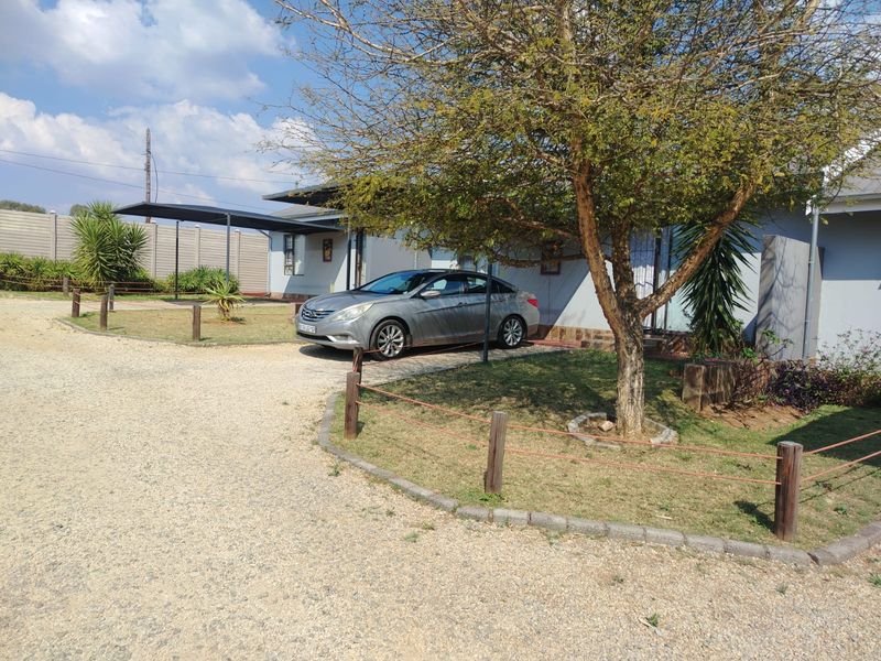Front exterior view of the property featuring a gravel driveway, carport, and established garden with timber fencing.