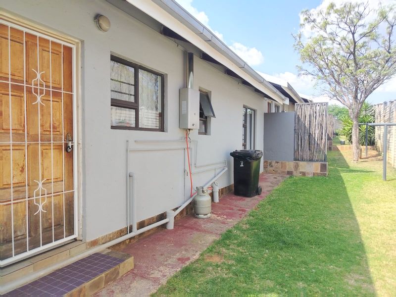 Rear exterior view of the property featuring a lawn, gas geyser installation, and a secure wooden entrance door with a metal security gate.
