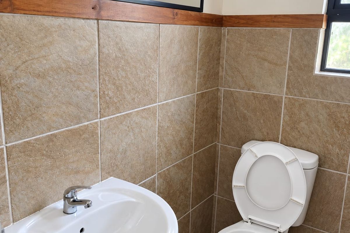 A clean, functional bathroom featuring a pedestal basin, toilet, and neutral tiled walls with timber trim detailing.