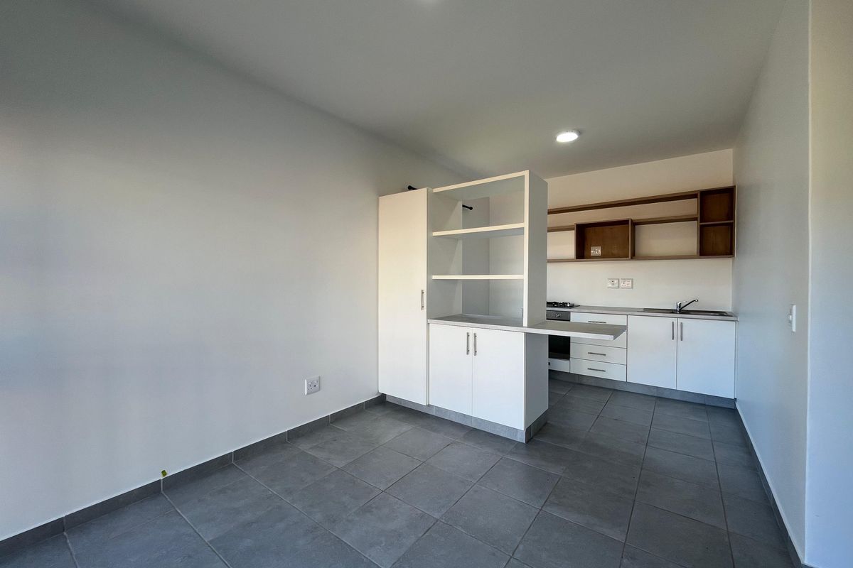 An open-plan kitchen area featuring modern white cabinetry, built-in oven and hob, tiled flooring, and a functional breakfast counter.