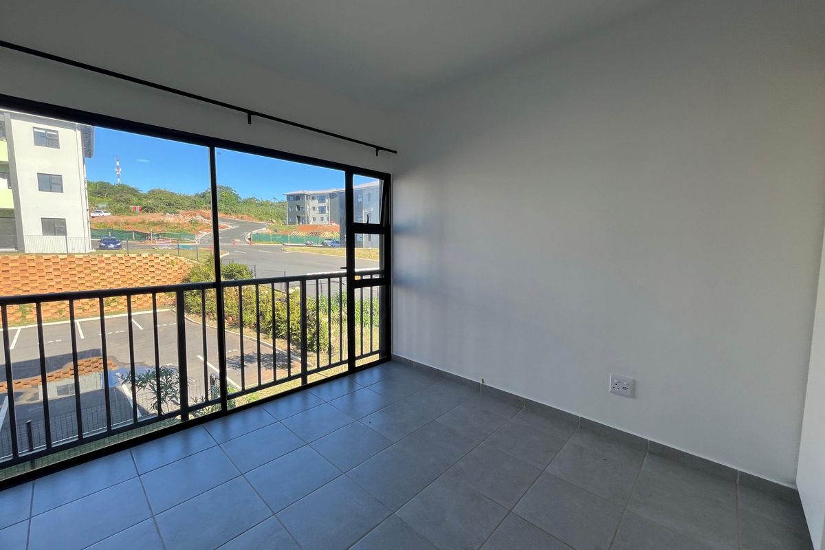 A bright, empty living area featuring large sliding glass doors that open onto a balcony with views of the surrounding estate.