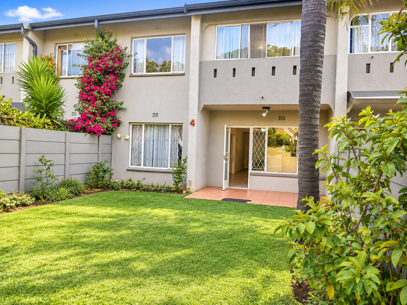 Rear view of the townhouse featuring a private garden, tiled patio area, and well-maintained exterior facade with established landscaping.