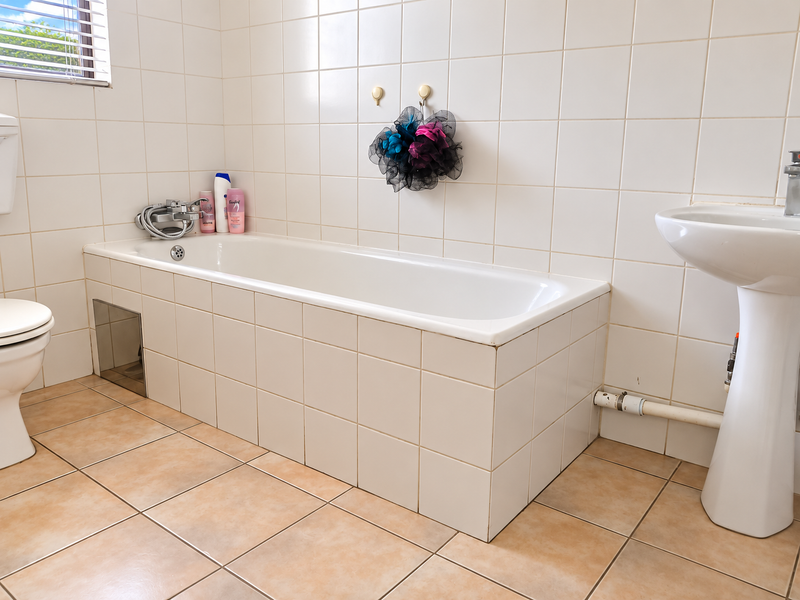 A functional bathroom featuring a tiled bathtub, pedestal basin, and toilet with neutral ceramic wall and floor tiles.