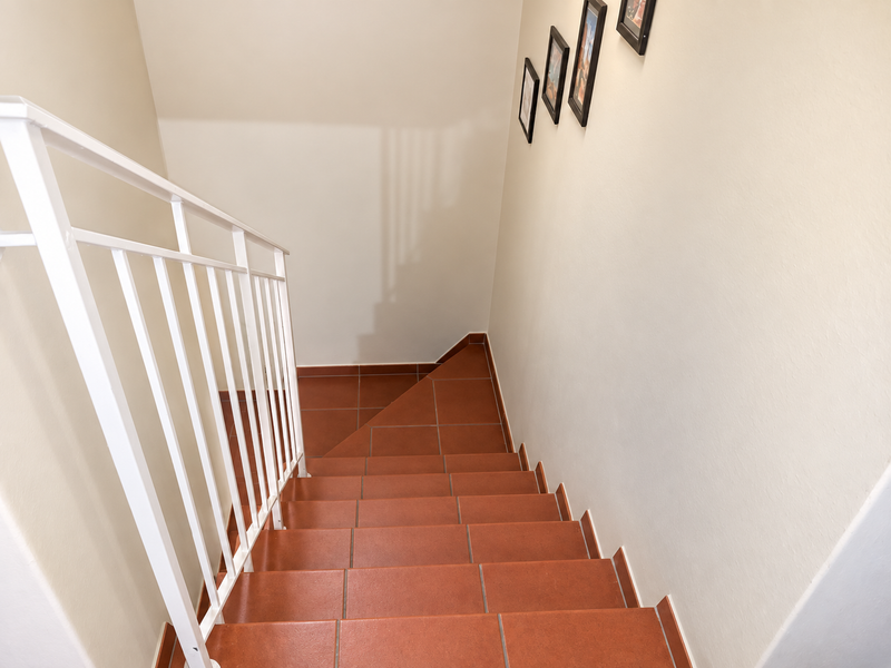 A clean staircase featuring terracotta-style floor tiles and a white metal balustrade, leading down to a lower level.