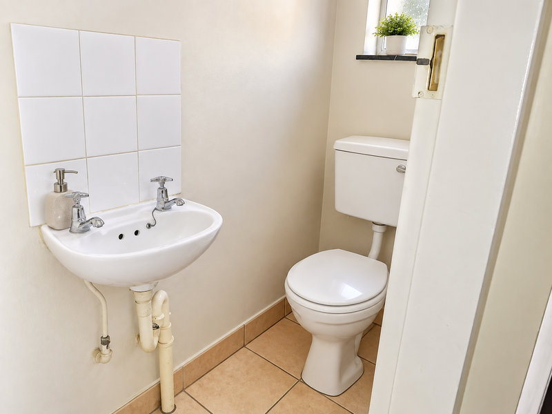 A compact guest bathroom featuring a wall-mounted basin with tiled splashback and a standard close-coupled toilet with neutral floor tiling.